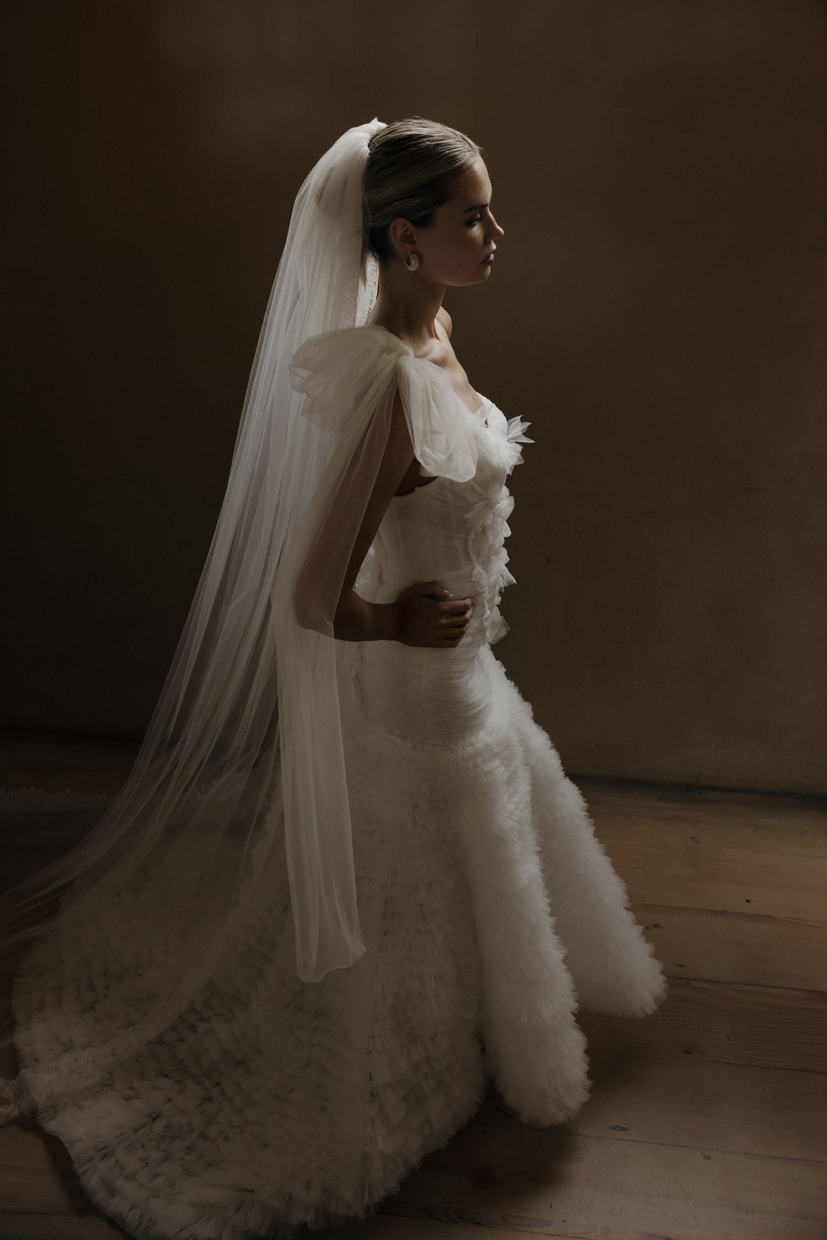 Bride in a textured gown with a floor-length veil, seen in profile