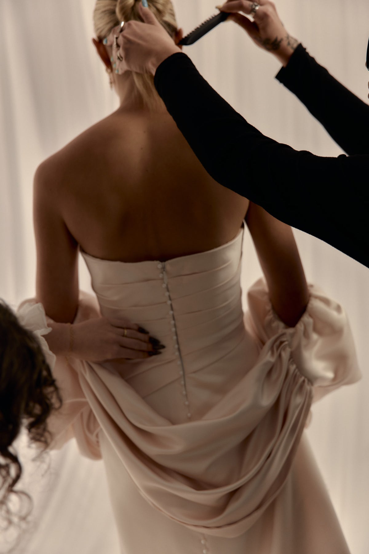 Back detail of a blush satin gown being fastened in the atelier